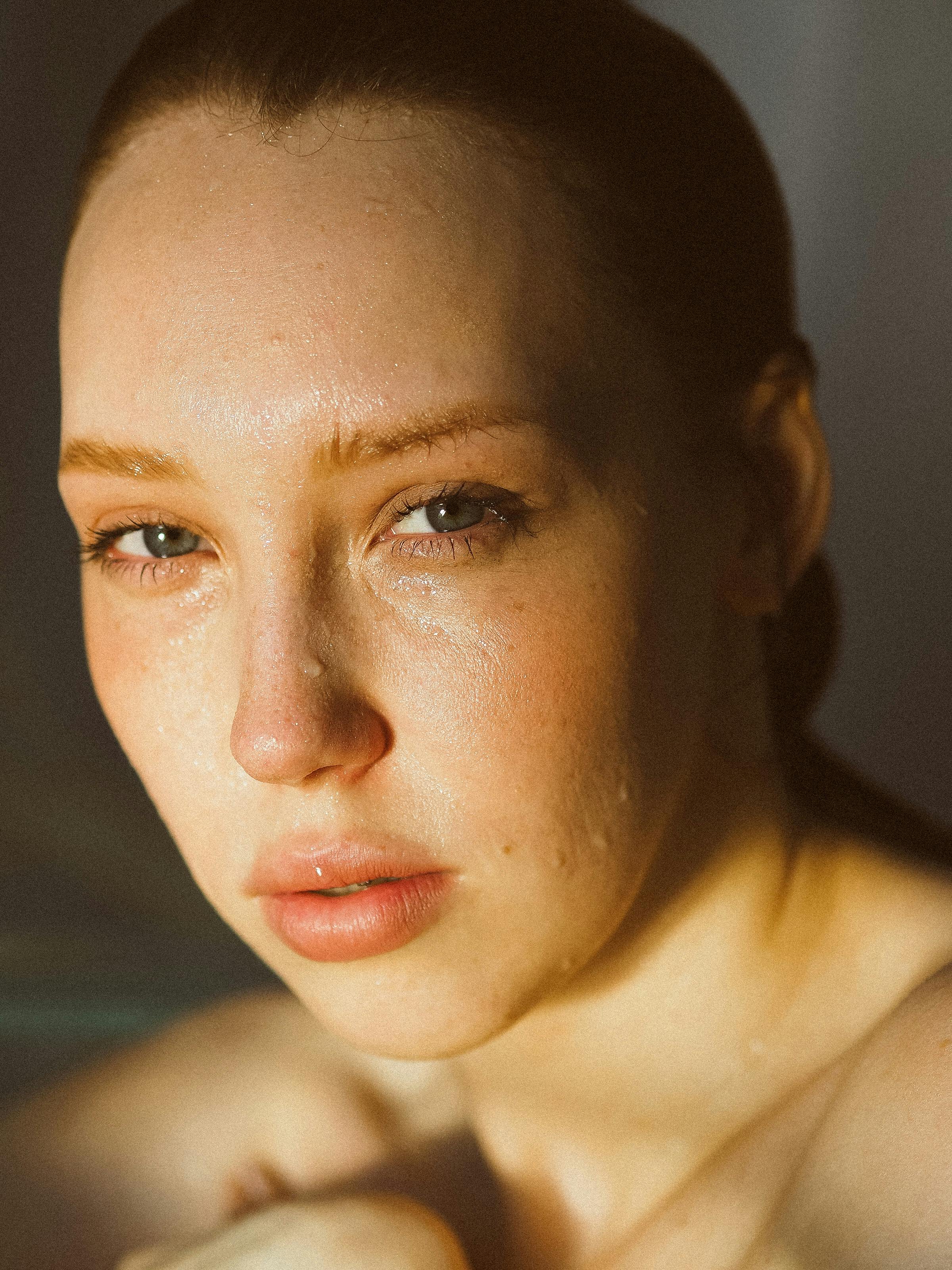 Close-up of a person with a shaved head and minimal makeup against a dark background